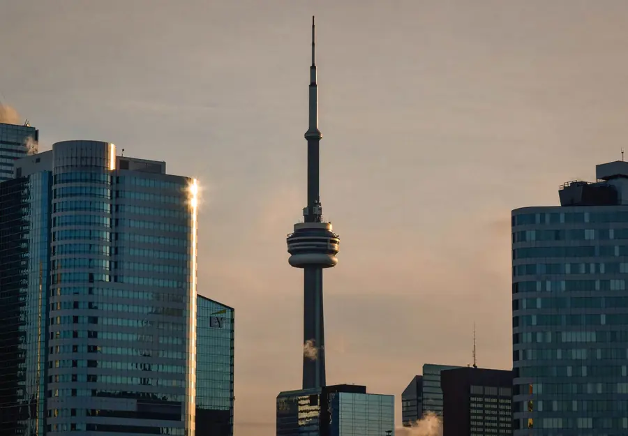 The CN Tower rising between glass office towers at dusk, with steam drifting off a rooftop vent in the foreground