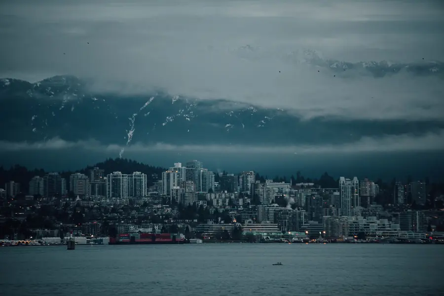 North Shore towers and container docks under low cloud, with snow on the mountains behind and the inlet in front